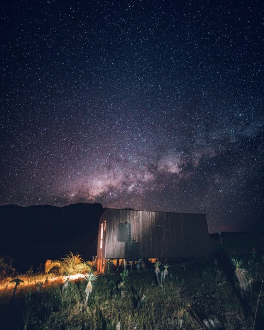 Via Láctea sobre a cabana iluminada, à noite